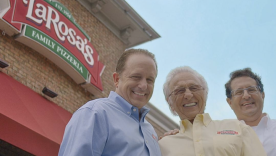 Three members of the LaRosa family pose in front of a LaRosa Pizzeria storefront.