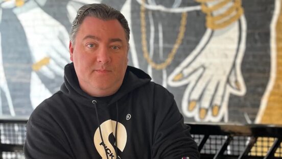 This photo shows Mike Burns wearing a black sweatshirt with the &pizza's trademark ampersand in gold lettering