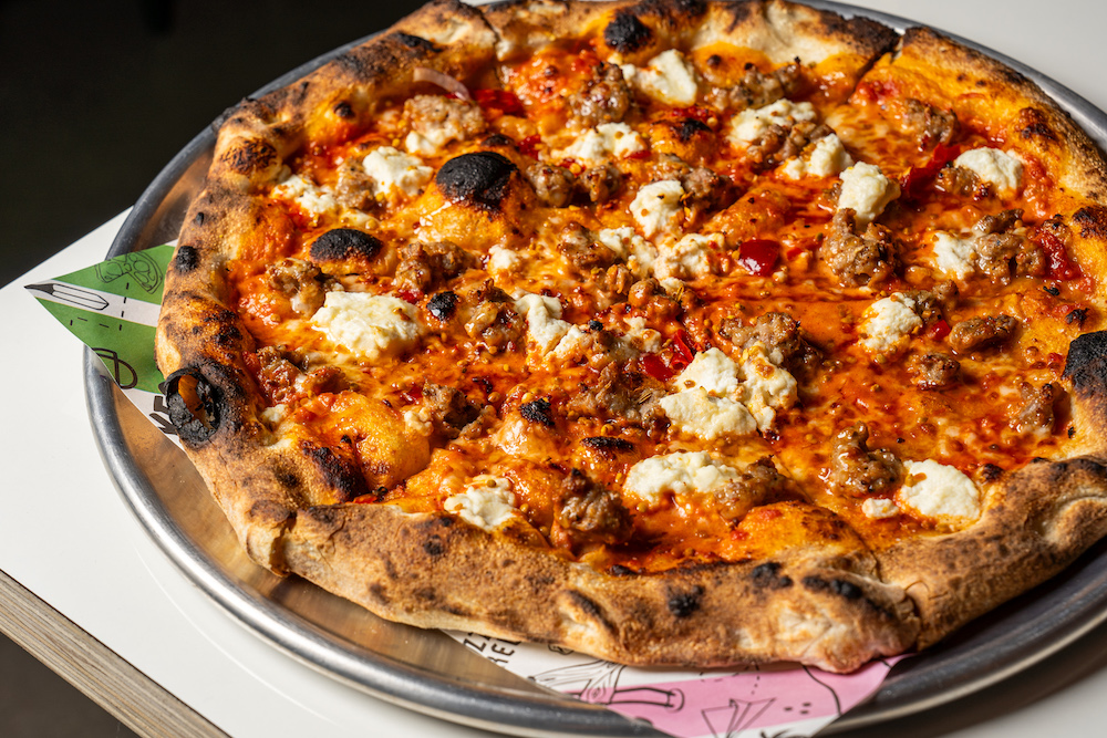 This photo shows a beautiful pizza topped with burrata, Italian sausage and other ingredients.