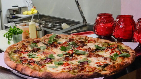 This photo shows a beautiful pizza placed in front of the make-line and flanked by three red candle jars.