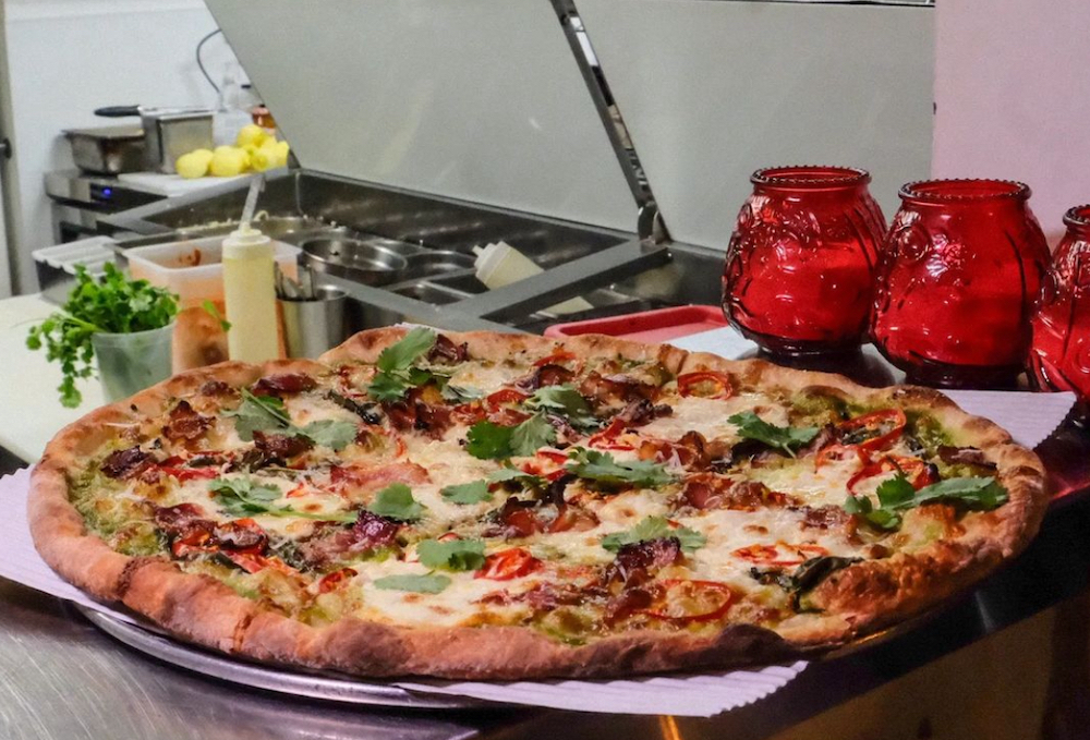 This photo shows a beautiful pizza placed in front of the make-line and flanked by three red candle jars.