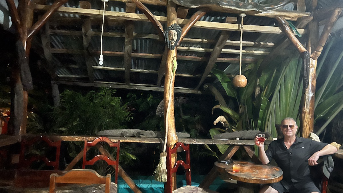 This photo shows Rudy Waldner sitting to the right side of a jungle-themed pizza restaurant. He is holding up a glass with some kind of red cocktail.