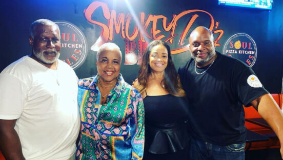 This photo shows the two owners of Soul Circles with two visiting women standing between them in front of a Smokey D'z BBQ sign.