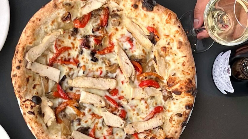 This photo shows a pizza topped with chicken, roasted red peppers, gorgonzola, mushrooms caramelized onions and smoked mozzarella