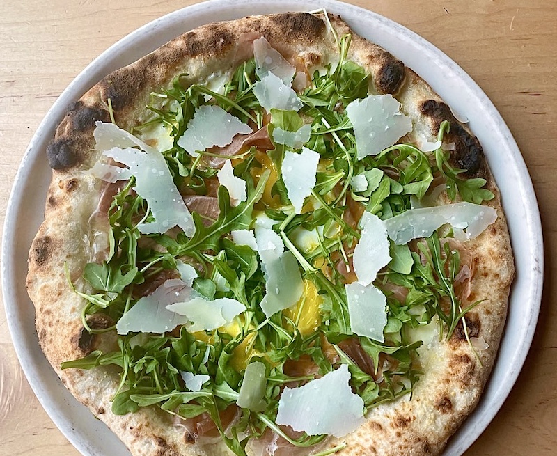 This photo shows a pizza topped with arugula, shaved Parmesan, prosciutto and other ingredients.