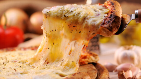 This photo shows a slice of pizza being extracted from a whole pie with a thick and scrumptious cheese pull.