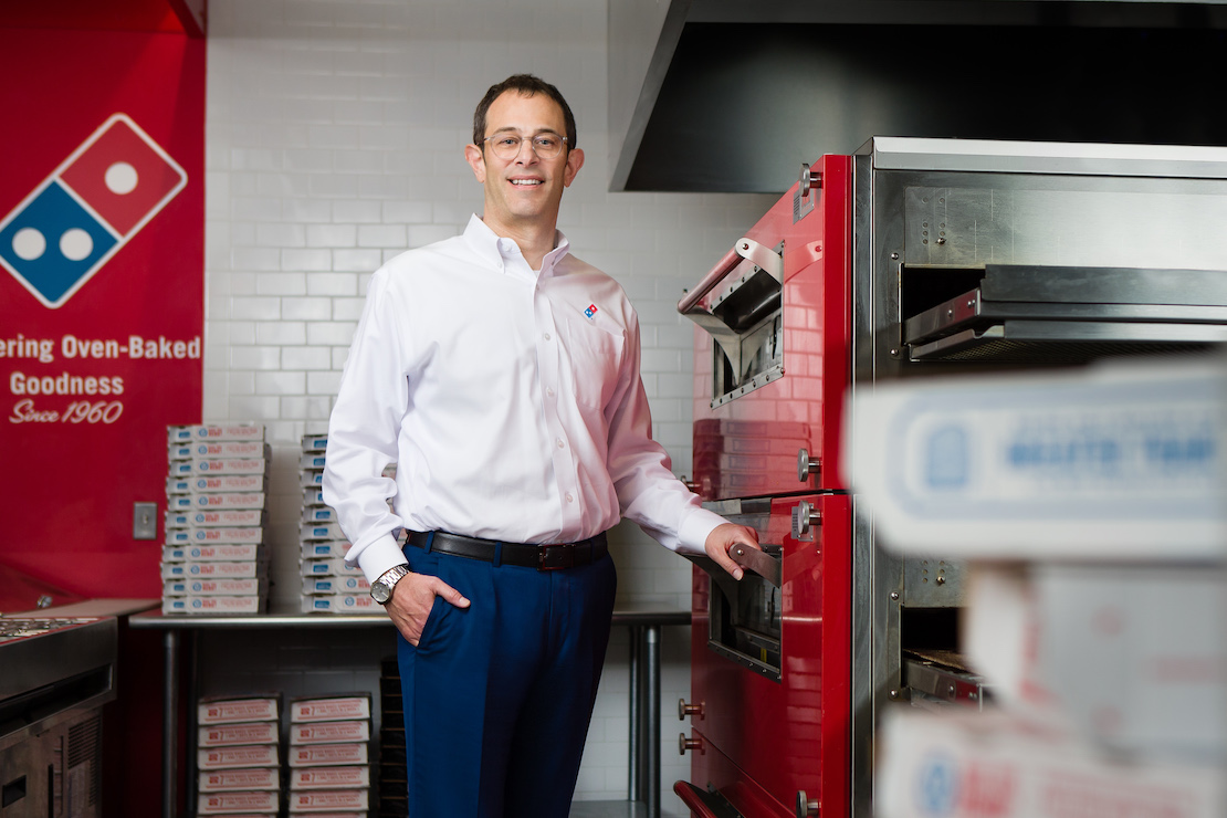 This photo shows Scott Wiener, wearing a white dress shirt and slacks, standing in a Domino's kitchen and smiling.