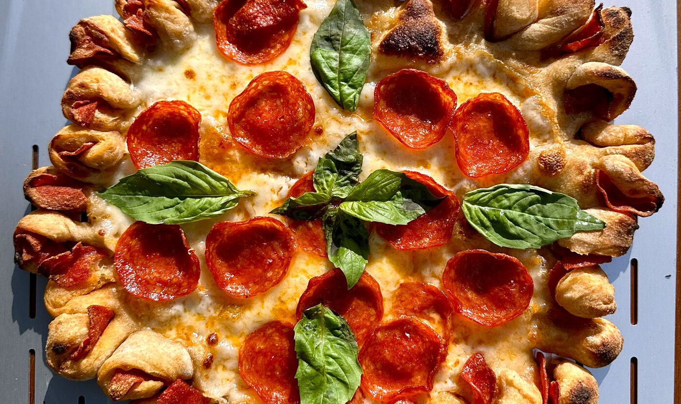 This photo shows a gorgeous pepperoni pizza with twisted and pinched, flower-like edges containing pepperoni slices.