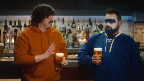 Two hockey fans stand in a bar, looking at one another suspiciously. The picture is part of Boston Pizza's new ad campaign designed to unite Canadian hockey fans.