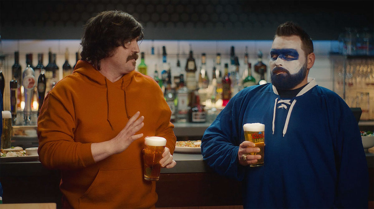Two hockey fans stand in a bar, looking at one another suspiciously. The picture is part of Boston Pizza's new ad campaign designed to unite Canadian hockey fans.