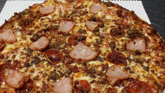 This photo shows a pizza topped with pepperoni, Canadian bacon, ground beef and possibly sausage.
