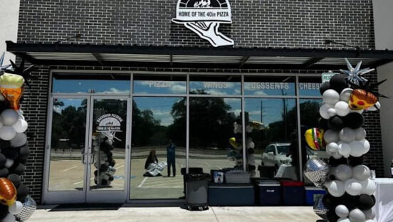 This photo shows the exterior of Backdoor Pizzeria with balloons on either side of the walkway heading toward the building.