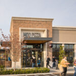 This photo shows the exterior of a MOD Pizza location with several customers, a little blurred, entering the story or walking away with their food.