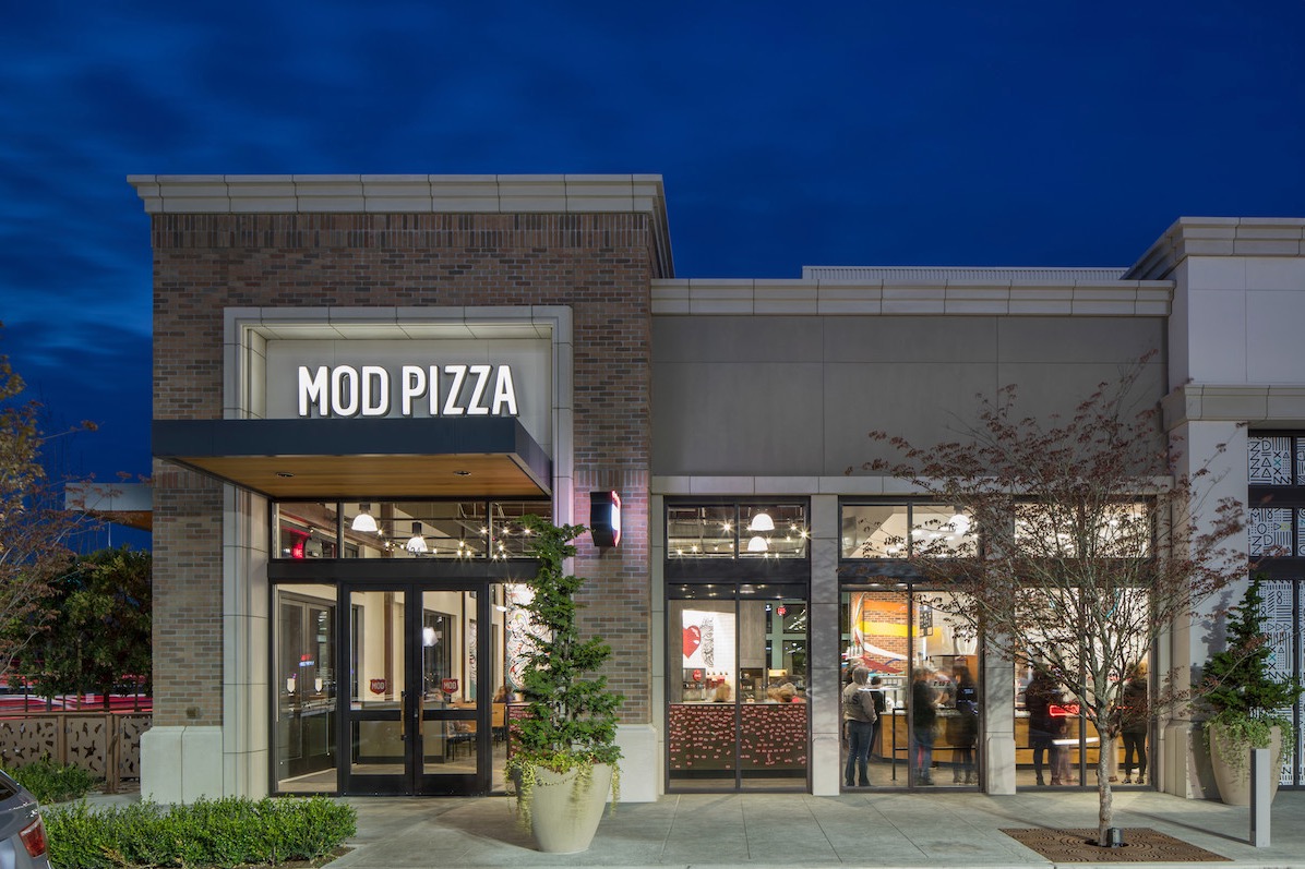 This photo shows a brightly lit MOD Pizza location against a dark blue backdrop.