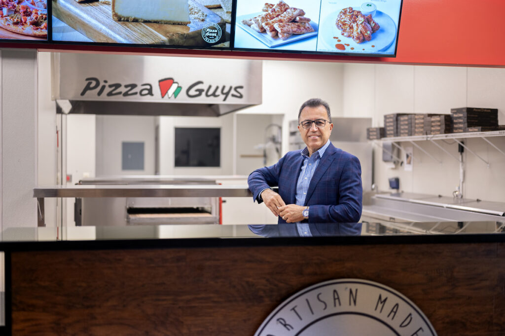 Shahpour Nejad poses behind the counter at Pizza Guys, the pizza franchise that he owns.