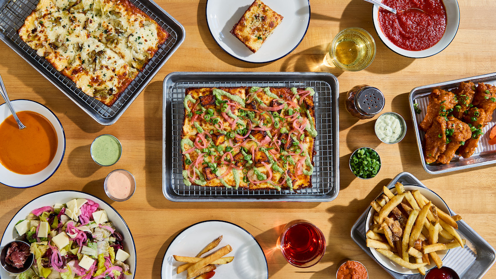 A paneer-style pizza in the middle of a large spread of food that includes other pizza, french fries, soup and more.