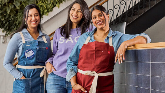 This photo shows three dark-haired women standing together and smiling.