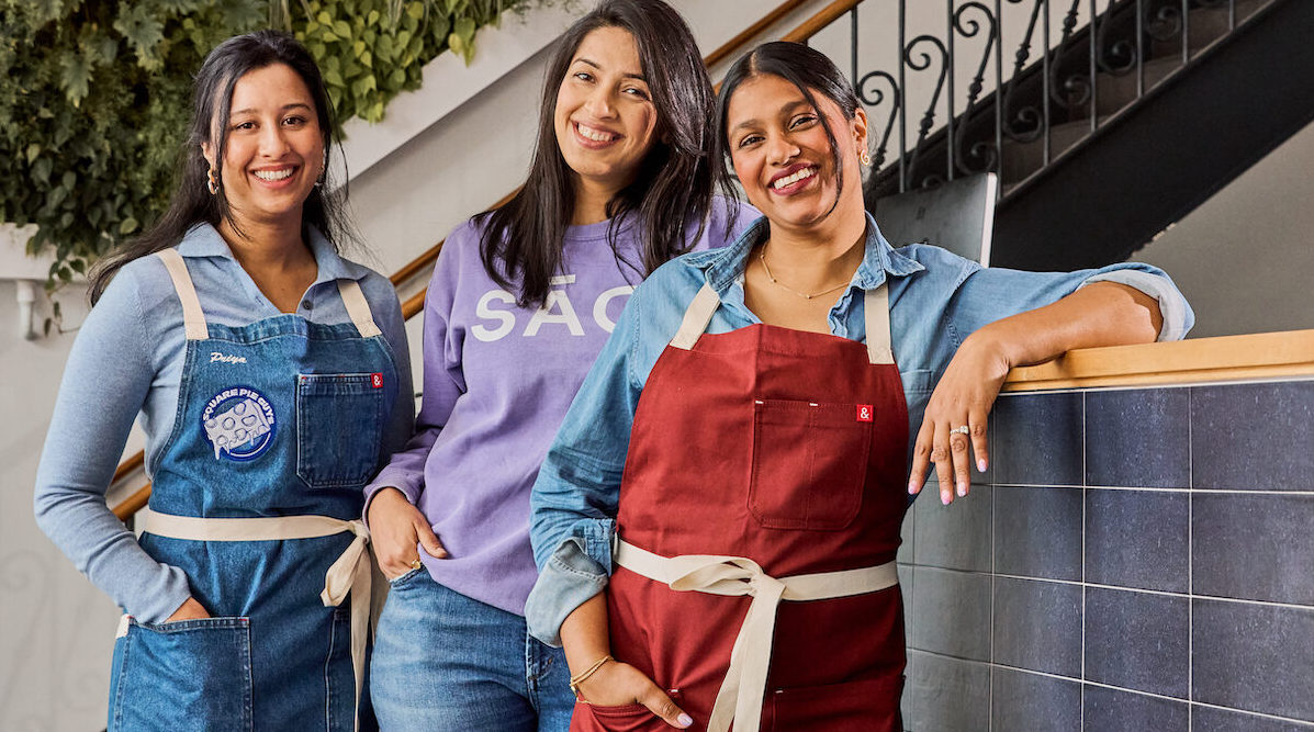 This photo shows three dark-haired women standing together and smiling.