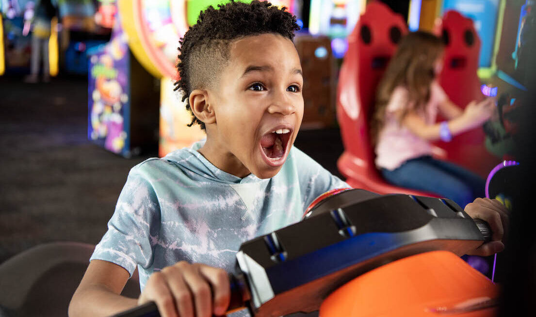 This photo shows a young boy looking excited as he plays some type of riding game on what looks like a kid-friendly motorcycle.