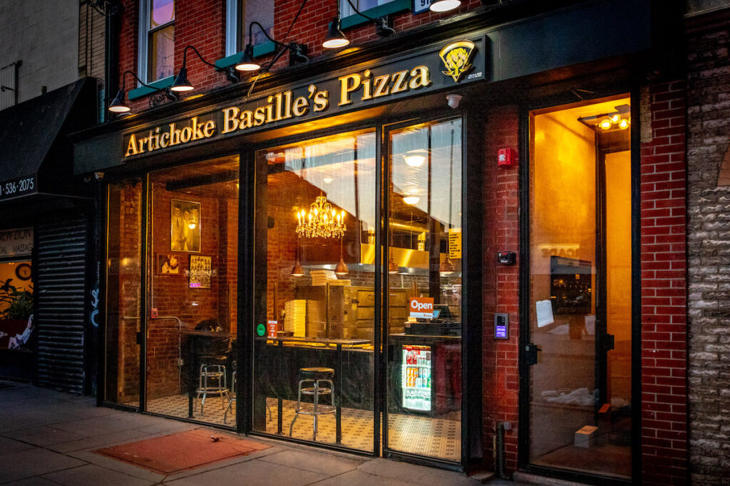 An exterior shot of a storefront at dusk: Artichoke Basille's Pizza in New York City.