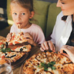 Happy mother and daughter eat pizza in a cafe and having fun.