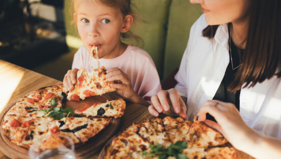 Happy mother and daughter eat pizza in a cafe and having fun.