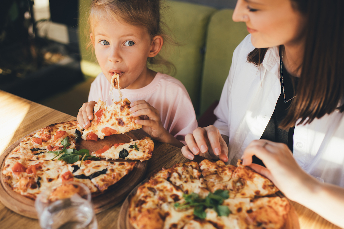 Happy mother and daughter eat pizza in a cafe and having fun.