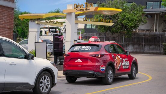 This photo shows a branded Pizza Hut delivery car in what looks like a McDonald's drive-thru.