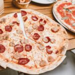 This photo shows two thin-crust pizzas, the most prominent one topped with sausage and pepperoni.