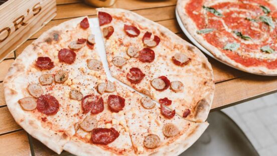 This photo shows two thin-crust pizzas, the most prominent one topped with sausage and pepperoni.