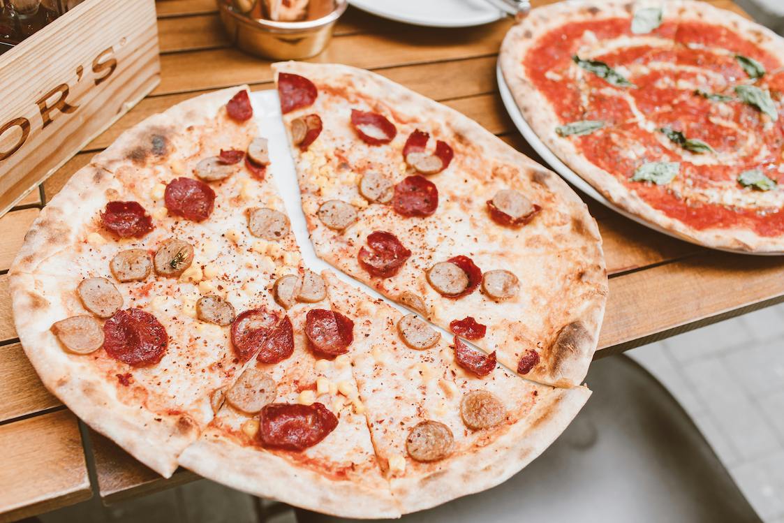 This photo shows two thin-crust pizzas, the most prominent one topped with sausage and pepperoni.