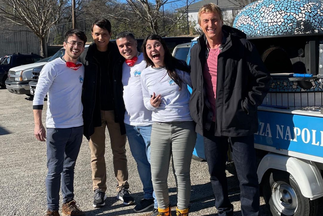 This photo shows Alessio Lacco and Sofia Arango posing in front of their beautiful blue pizza vehicle with actors Ralph Macchio and William Zabka.