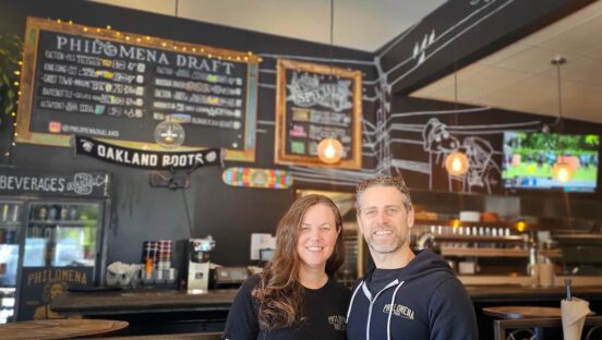 This photo shows the husband-and-wife owners of Philomena smiling at the camera with their restaurant's beer board in the background.