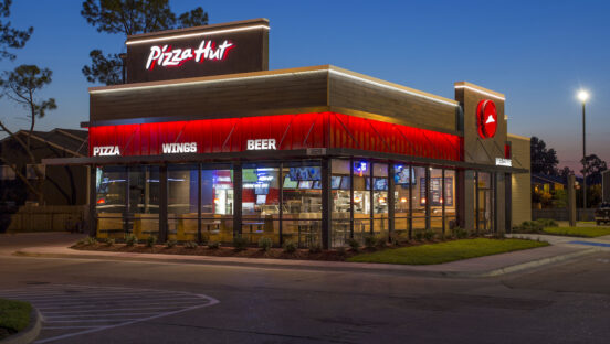 This photo shows the brightly lit exterior of a Pizza Hut restaurant against a dark blue sky.