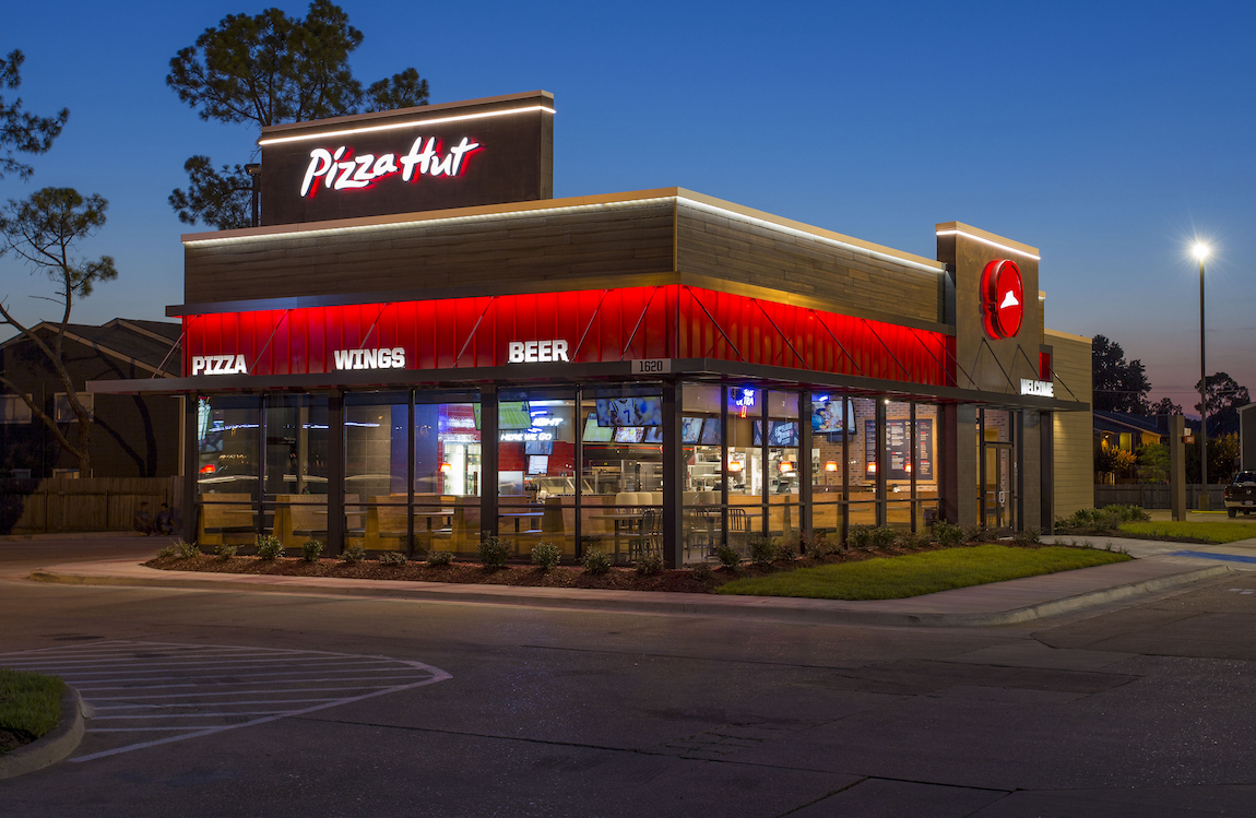 This photo shows the brightly lit exterior of a Pizza Hut restaurant against a dark blue sky.