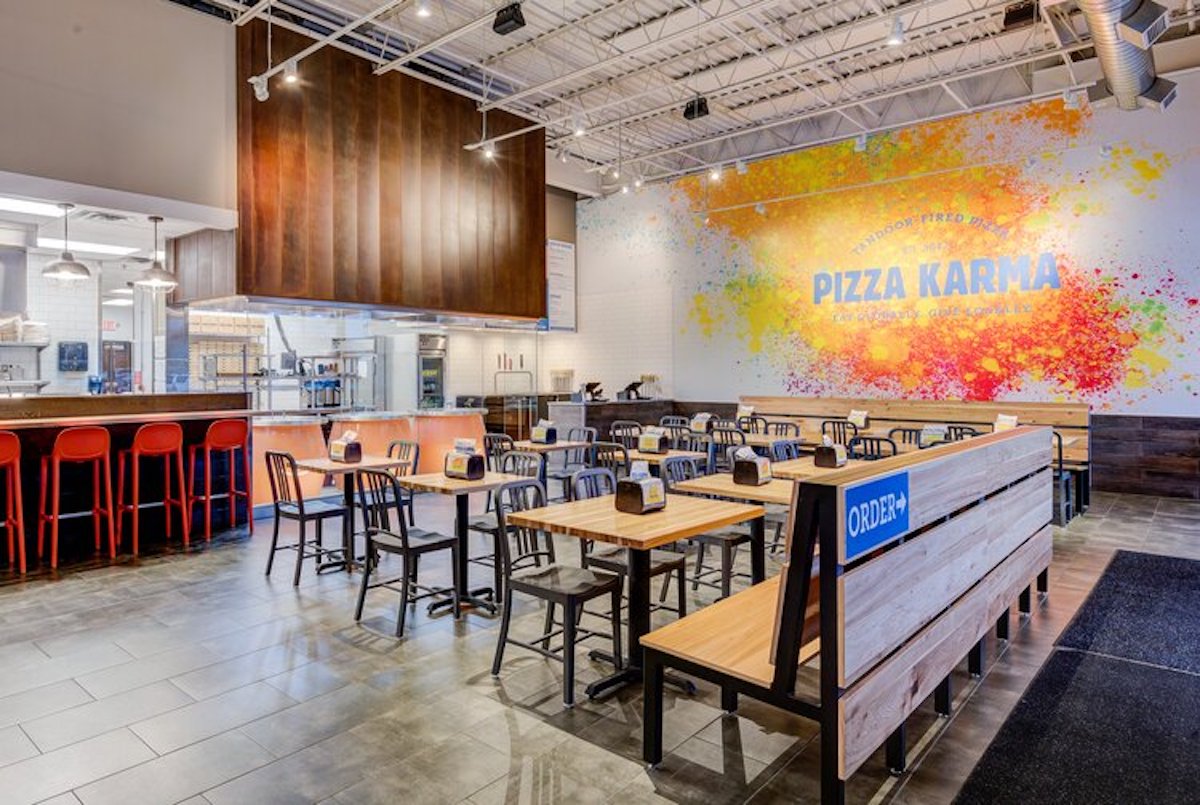 The inside of a Pizza Karma storefront, with sleek walls and tables and a Pizza Karma logo on the wall.