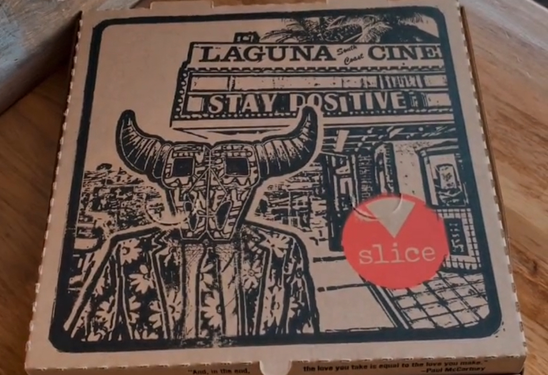 This photo shows an artist-designed pizza box featuring a mysterious horned figure with square eyes.