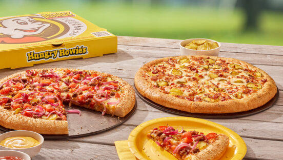 Two pizzas sit atop a picnic table in a summer scene.