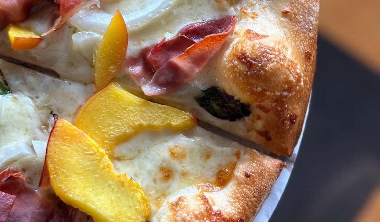 This photo shows a specialty pizza topped with peaches, prosciutto, Vidalia onions and other ingredients.