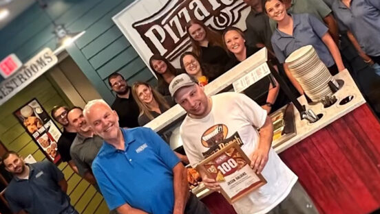 This photo shows Pizza Ranch's superfan with members of the executive team, who have given him a certificate for visiting his 100th location.