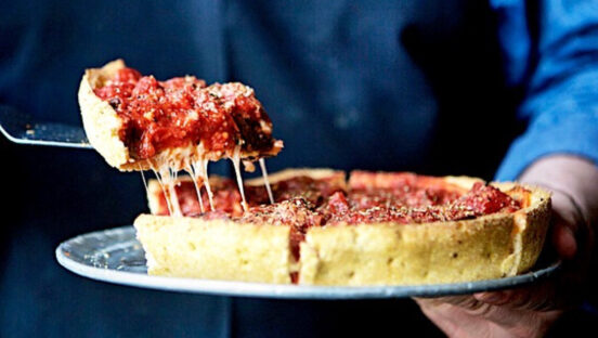 This photo shows someone removing a slice of deep-dish pizza from a whole pie at Pi Pizzeria.