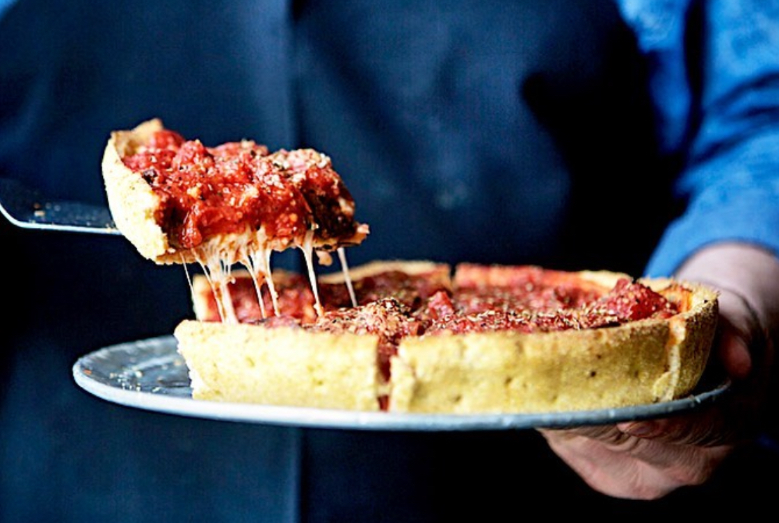 This photo shows someone removing a slice of deep-dish pizza from a whole pie at Pi Pizzeria.