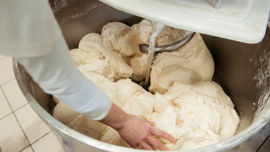 This photo shows a baker preparing dough in a dough mixer.