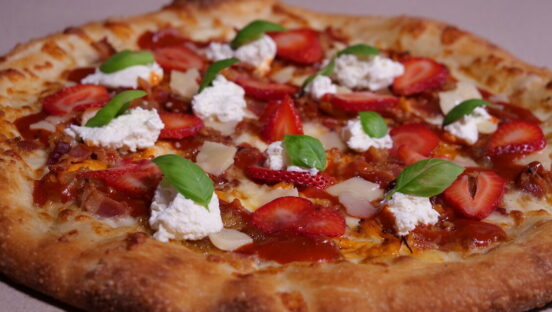 This photo shows a beautiful pizza topped with chicken, strawberries, dollops of whipped cream cheese, a sriracha strawberry glaze, and mozzarella and Parmesan cheeses.