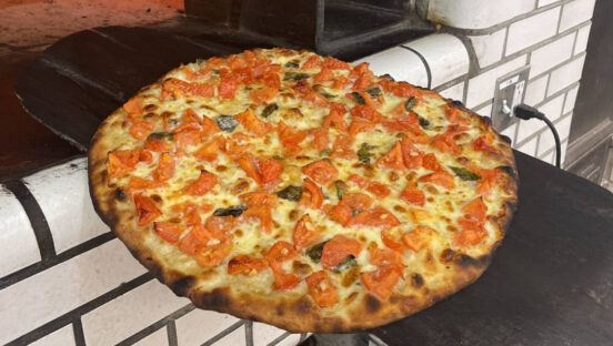 This photo shows a fresh tomato pie coming out of the oven at a Frank Pepe location.