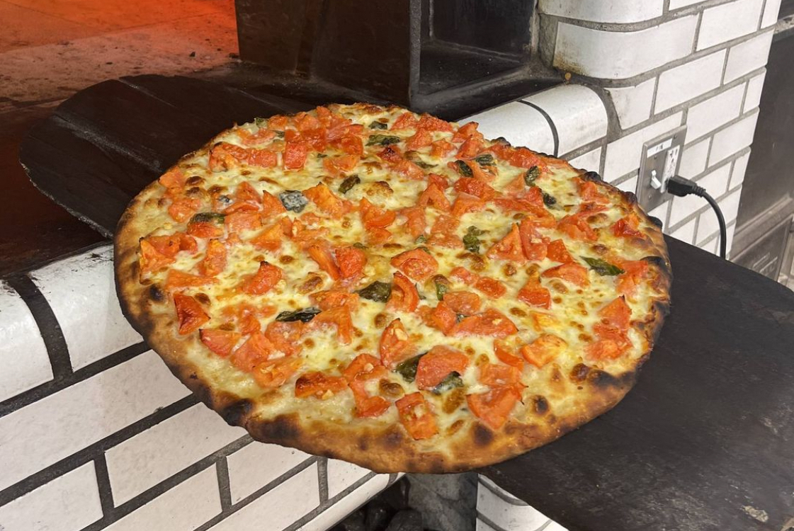 This photo shows a fresh tomato pie coming out of the oven at a Frank Pepe location.
