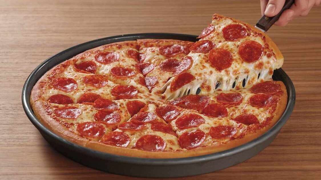 This photo shows someone's hand using a spatula to pull a slice of deep-dish pizza from a pan.