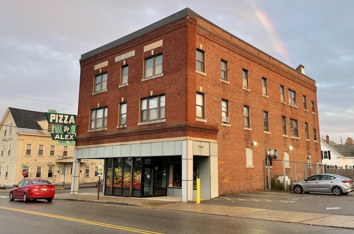 Pizza by Alex, a pizzeria in downtown Biddeford, Maine, sits on Main Street with a rainbow behind it.
