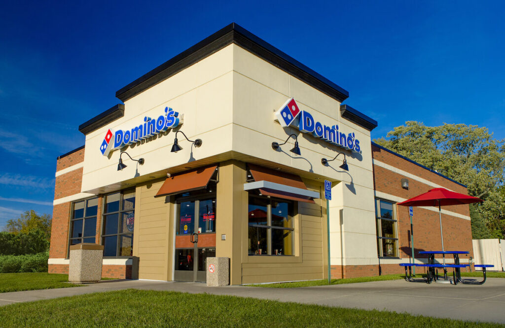 A Domino's storefront in Lansing, Michigan, with a brilliant blue sky behind it.