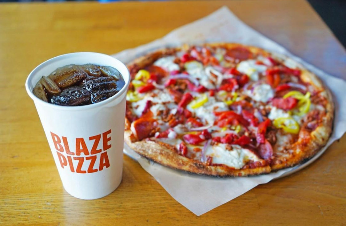 This photo shows a thin-crust pizza with red peppers and cheese and a beverage cup with the Blaze Pizza logo.